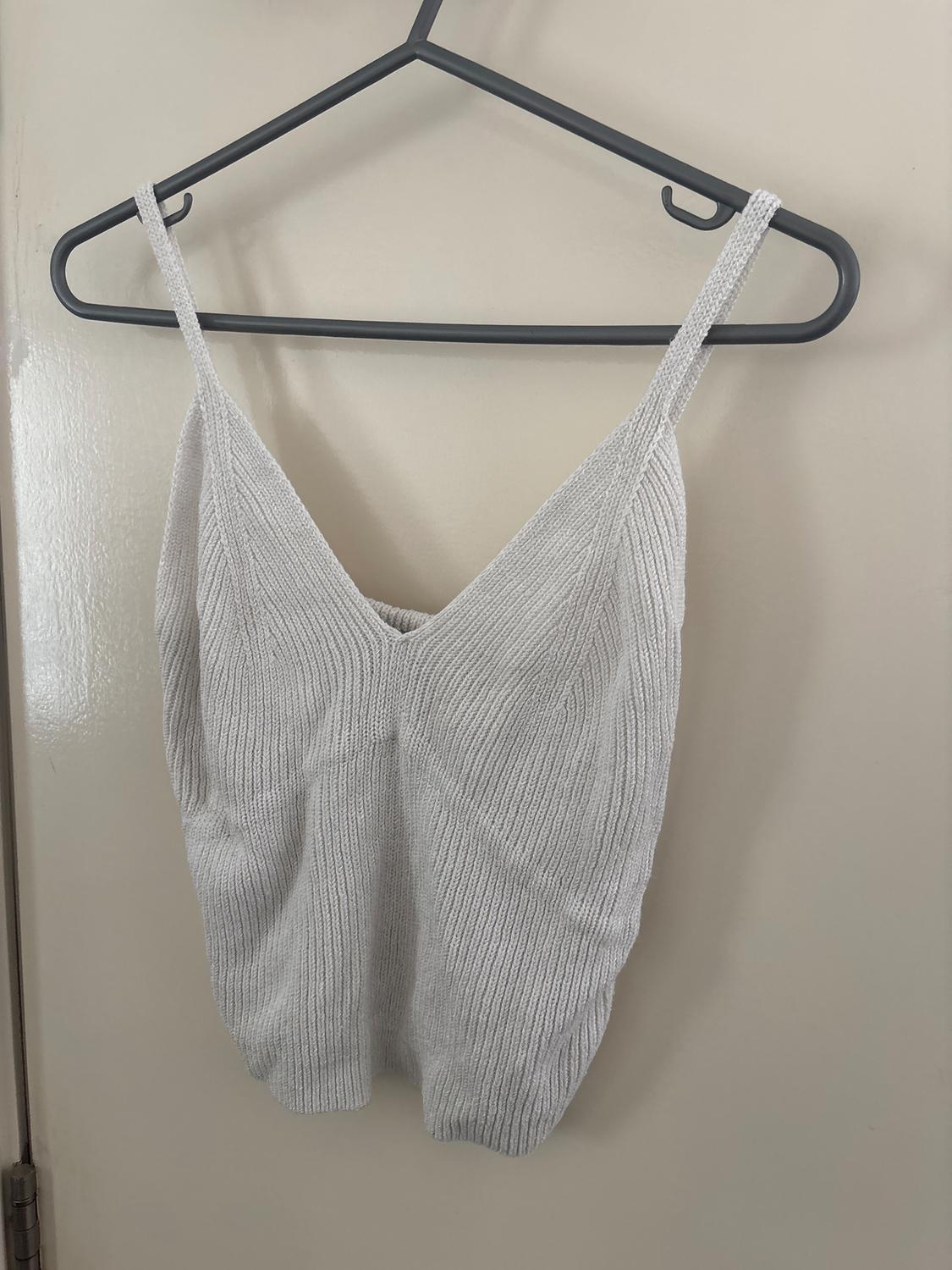 Light grey woven camisole top hanging on a black hanger over a white door.