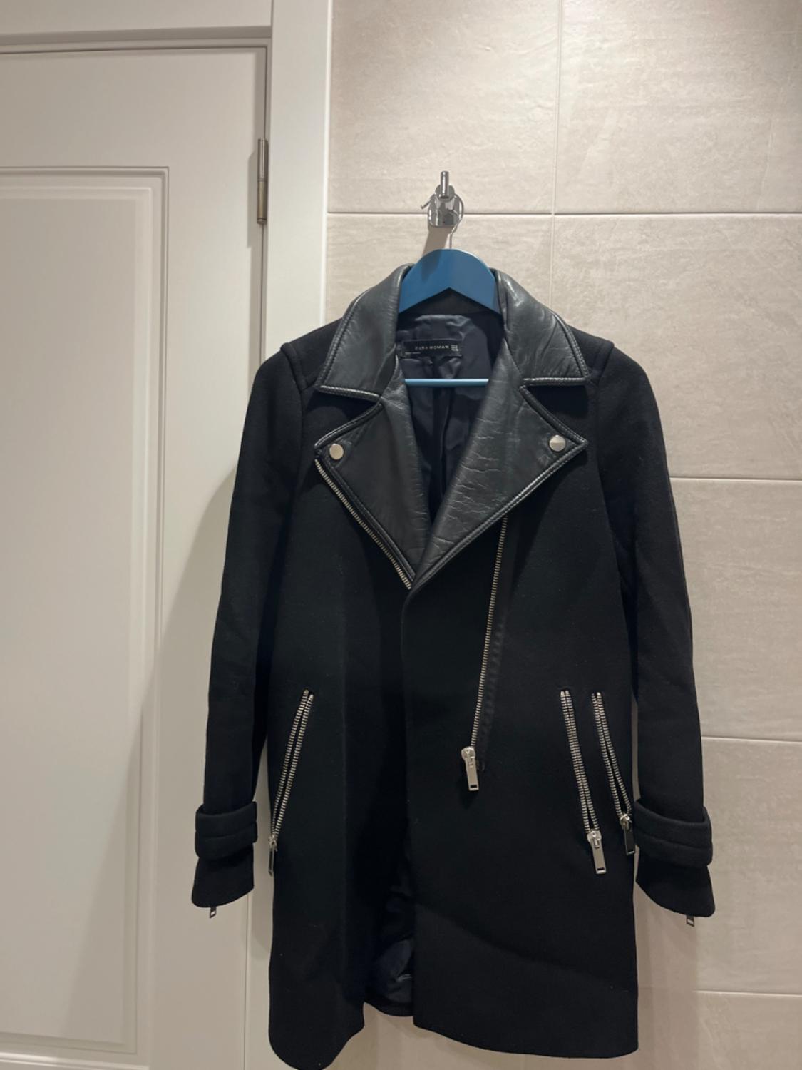 Front view of a black coat with zips and a faux fur collar.