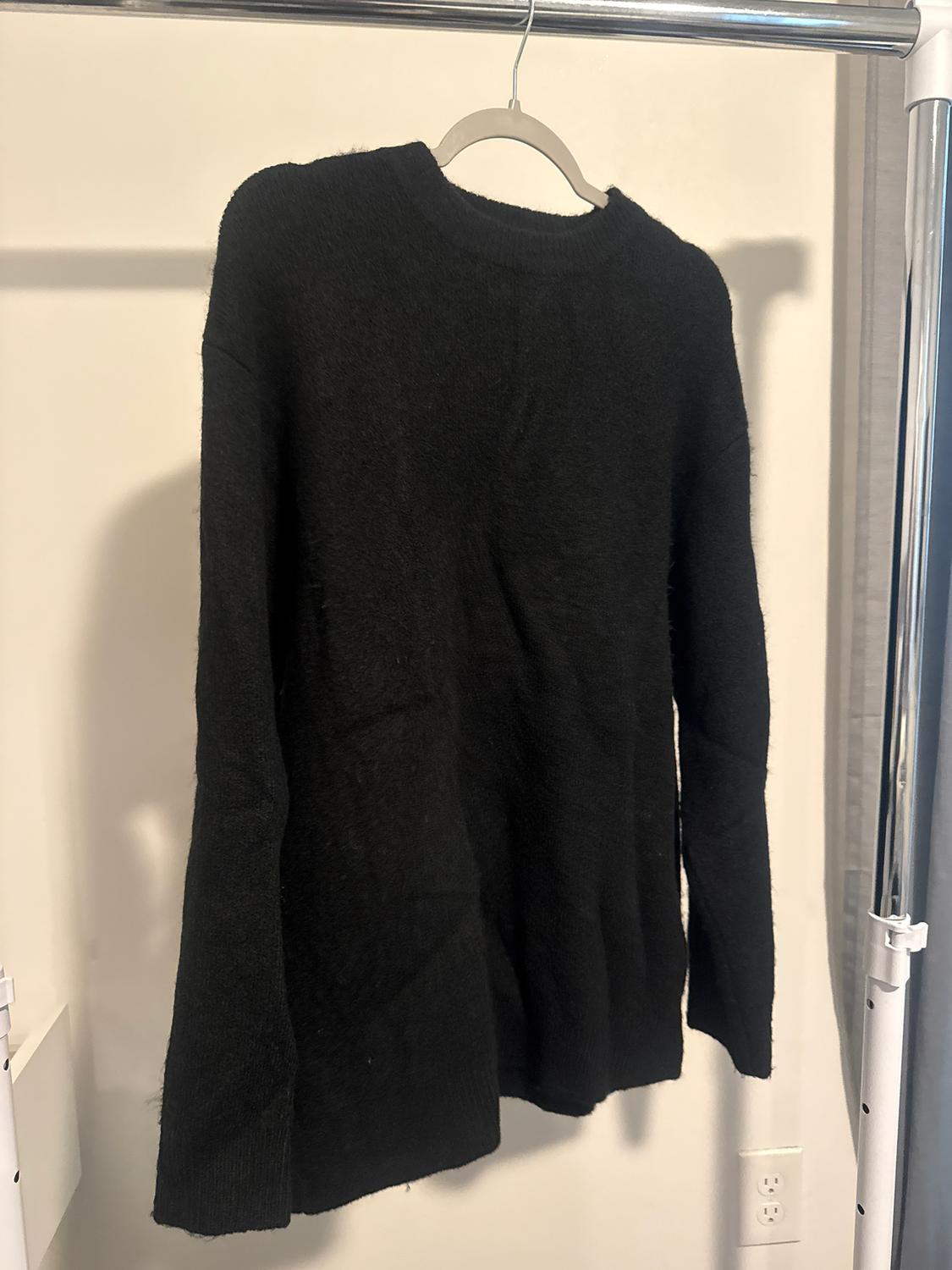 Black long-sleeved jumper hanging on a hanger against a white background. The texture appears soft and cosy.