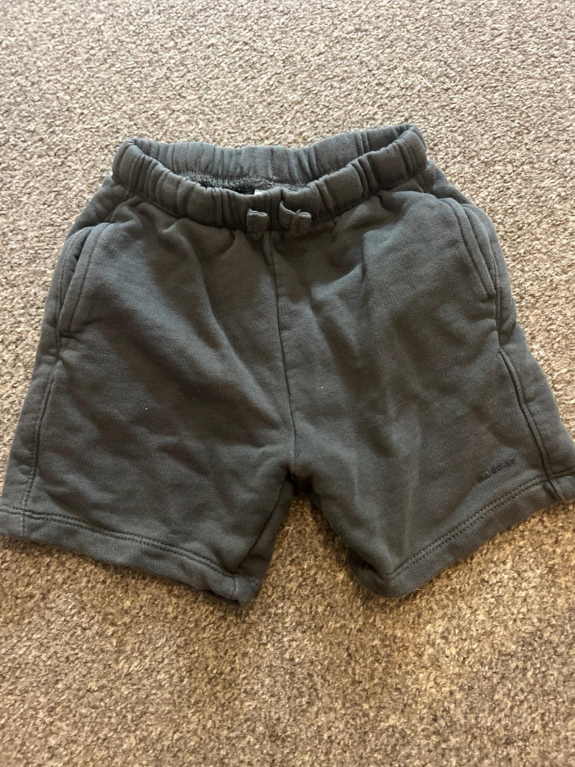 Dark grey sweat shorts with an elasticated waistband, drawstring detail and pockets, on a beige carpet.