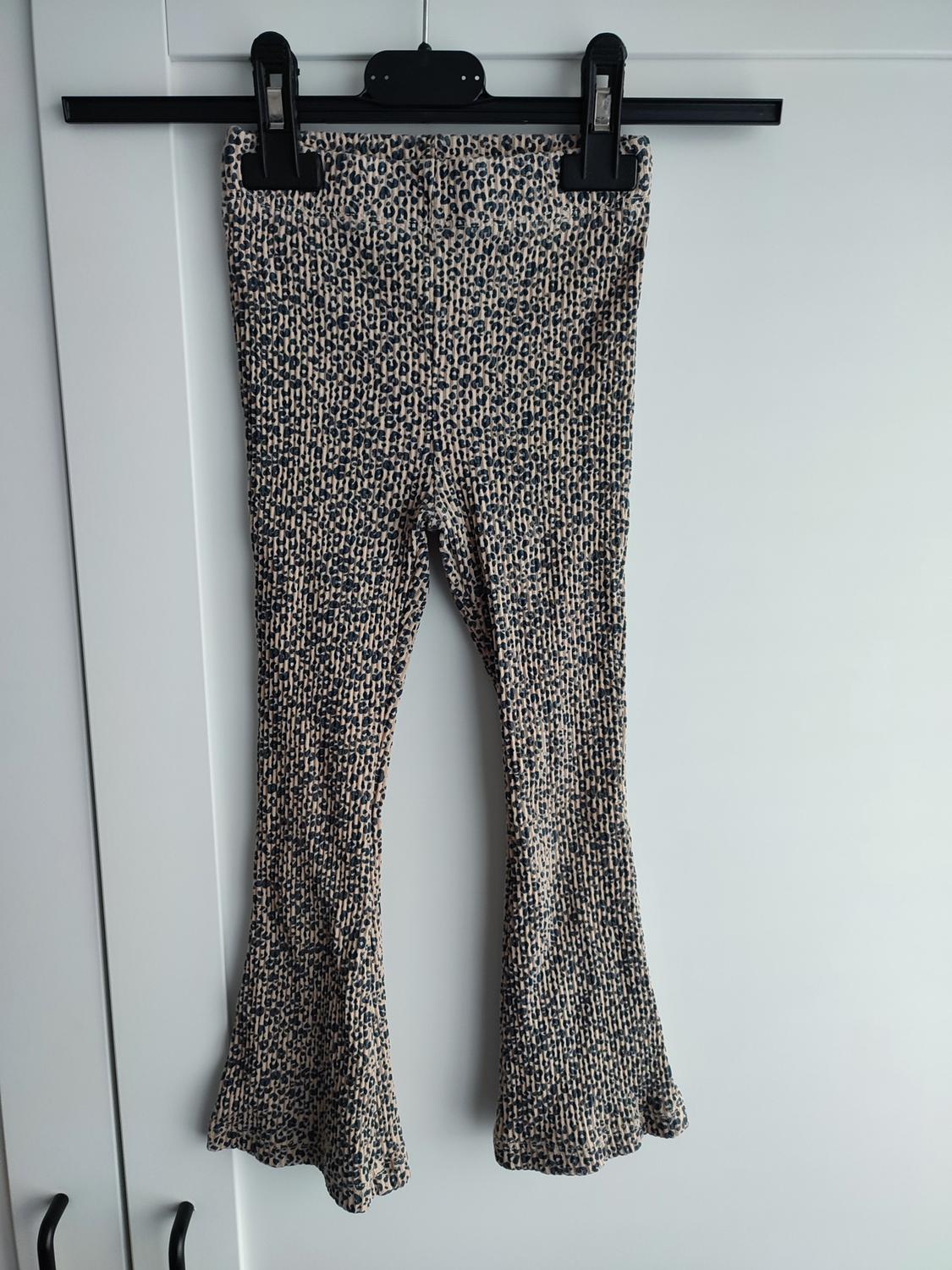 Flared ribbed trousers with an animal print, hanging on a black coat hanger over a white door.