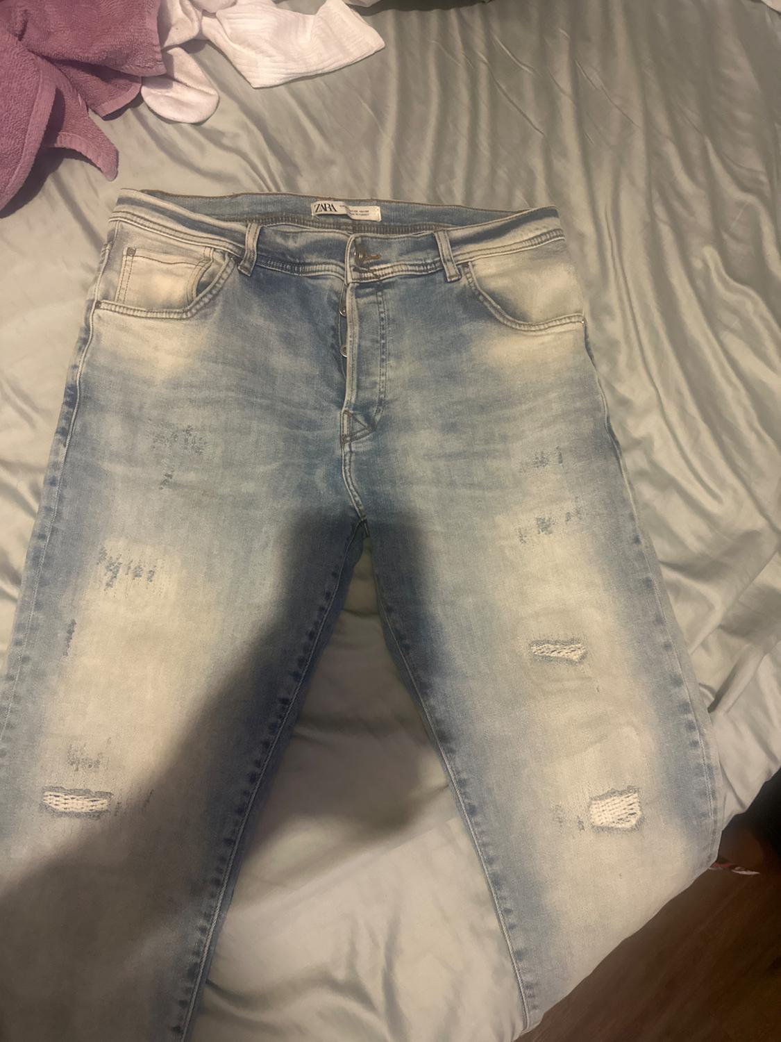 Light blue, distressed and ripped ZARA jeans on a bed with grey sheets.