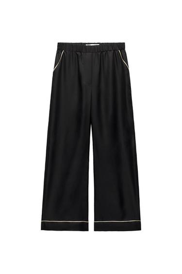 Fluid black trousers with an elasticated waist and light-coloured trims on the pockets and hem, against a white background.