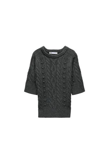 Grey knitted jumper with cable knit design and short sleeves. Visible label with "ZARA" text on the neck. White background.