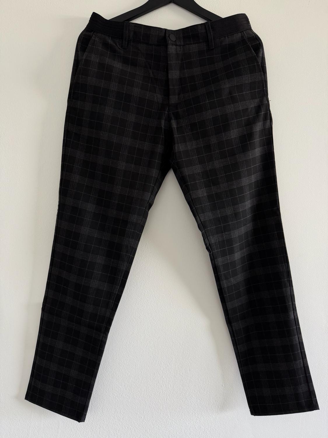Black plaid pants hanging on a black hanger against a white wall.