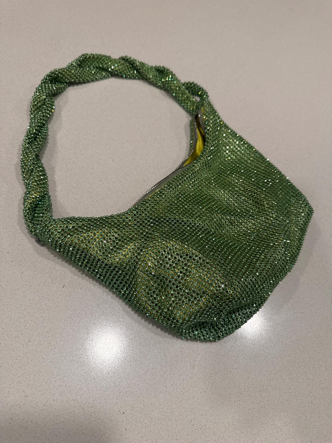 Bright green bag with a mesh texture on a light surface. The handle has a braided design.