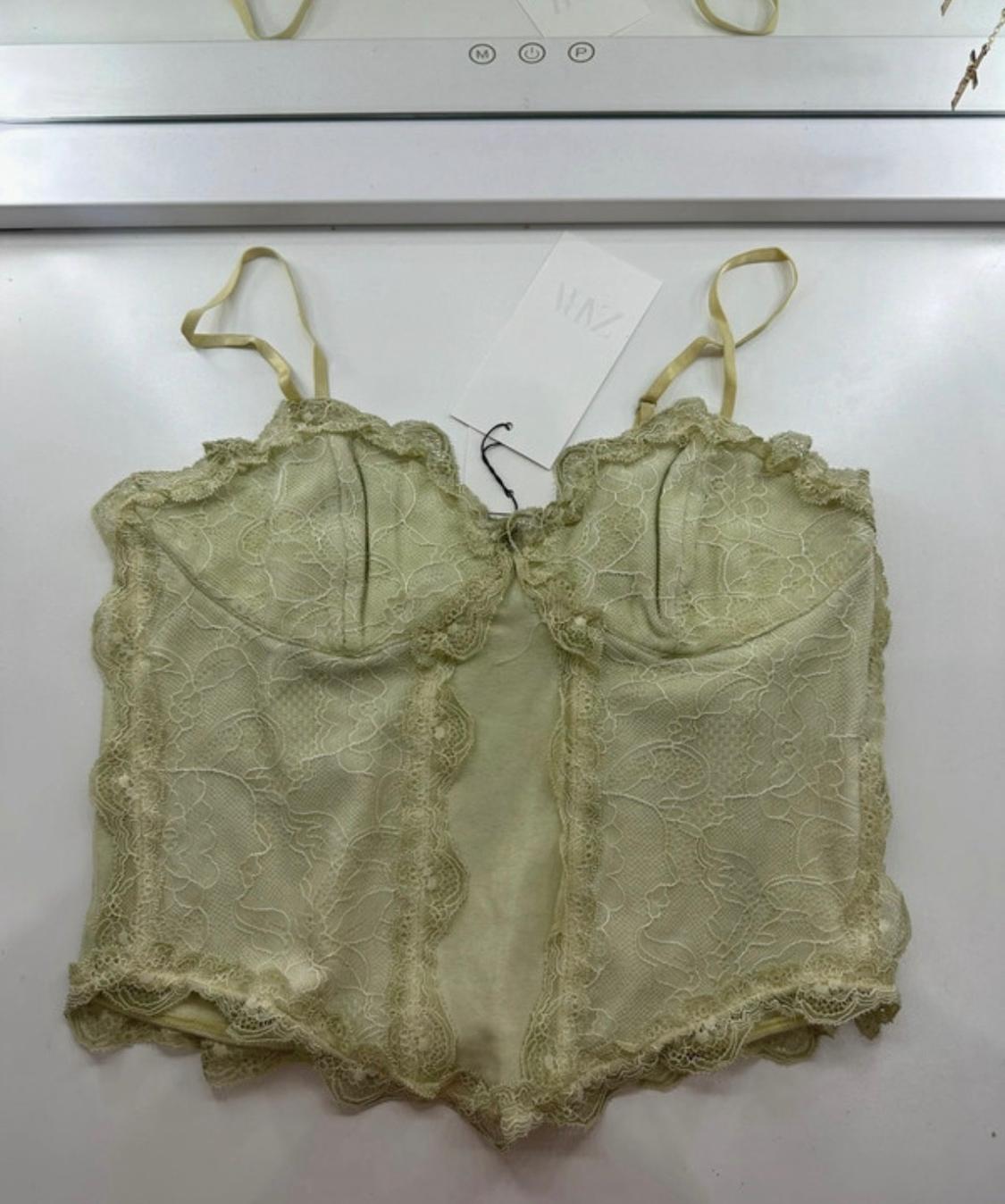 Light green lace corset top on a white surface. Label with ZARA text. Upper edge with letters M and P.