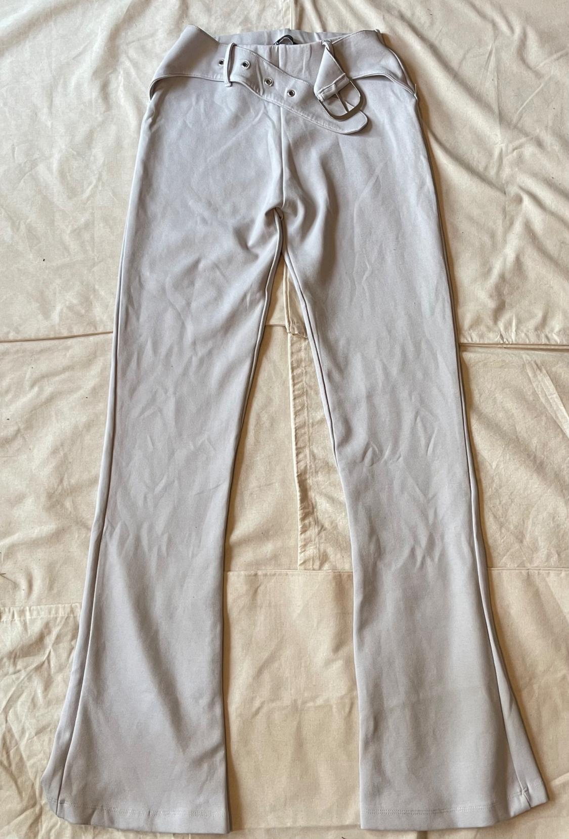 Light gray flared pants with a matching belt and silver buckle, laid out on beige fabric with stitching.