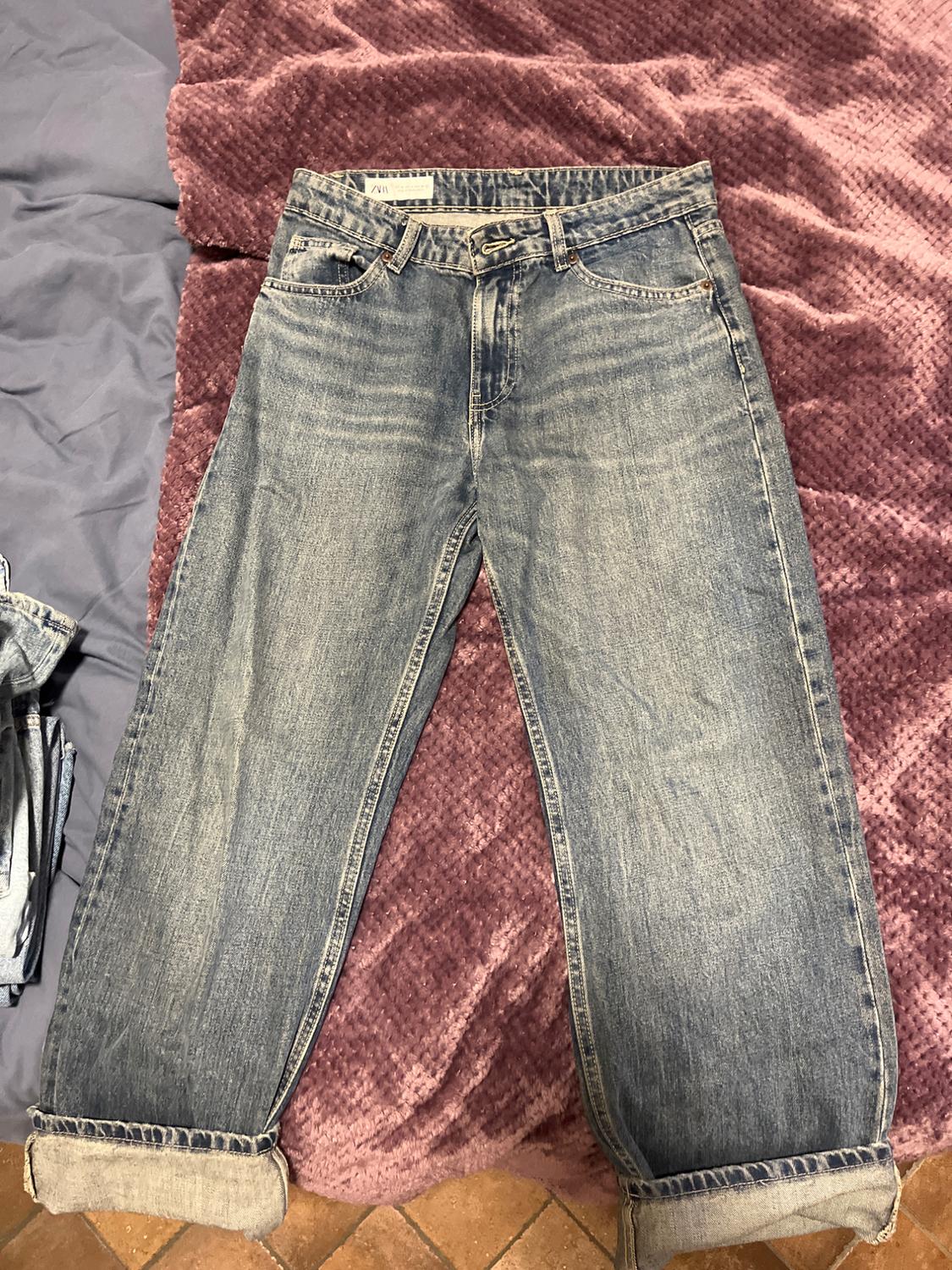 Worn blue jeans with rolled hem, placed on a purple textured blanket. Visible label on the waistband.