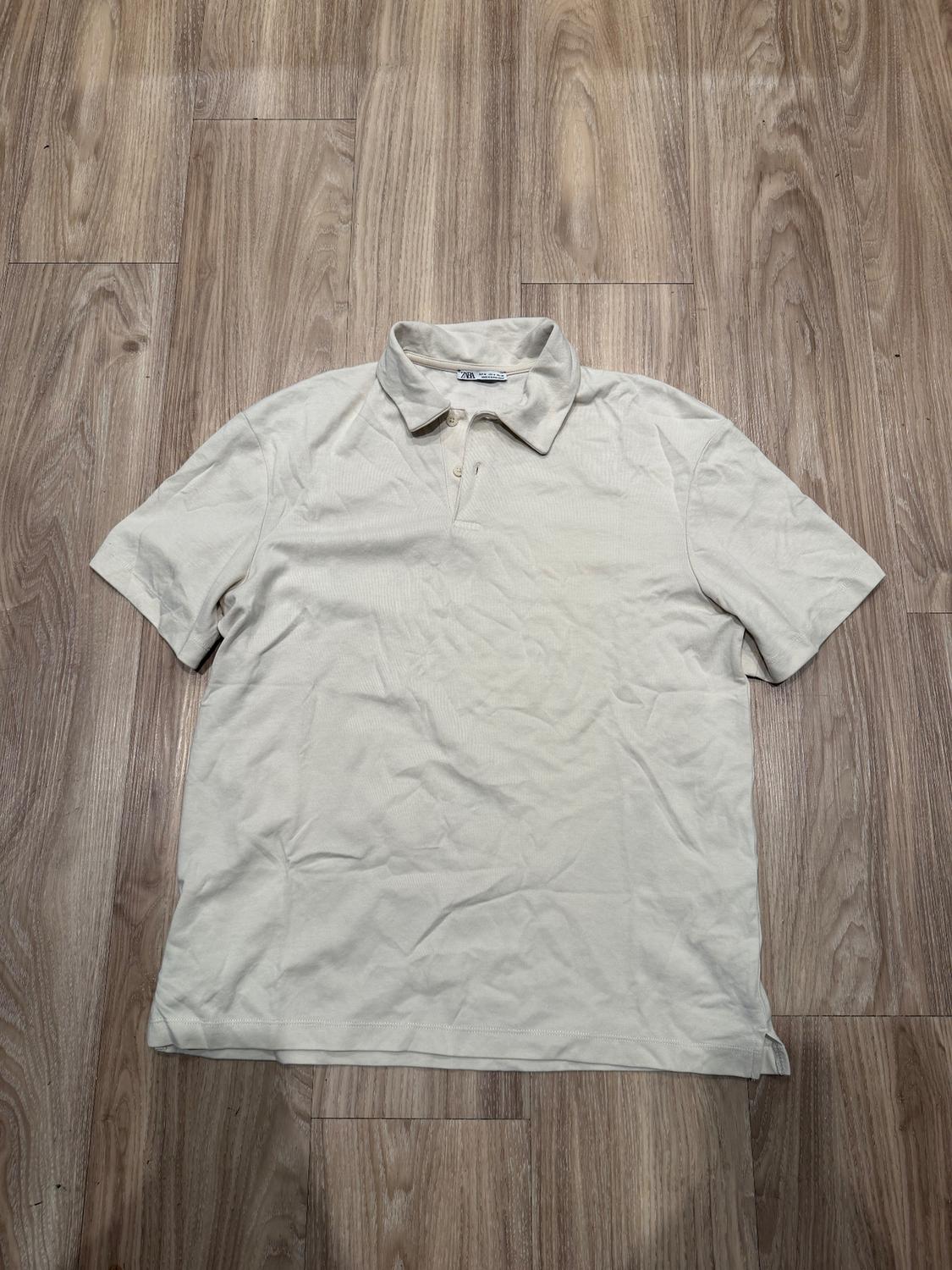Creased beige polo shirt on a light wooden floor. Label visible on the collar.