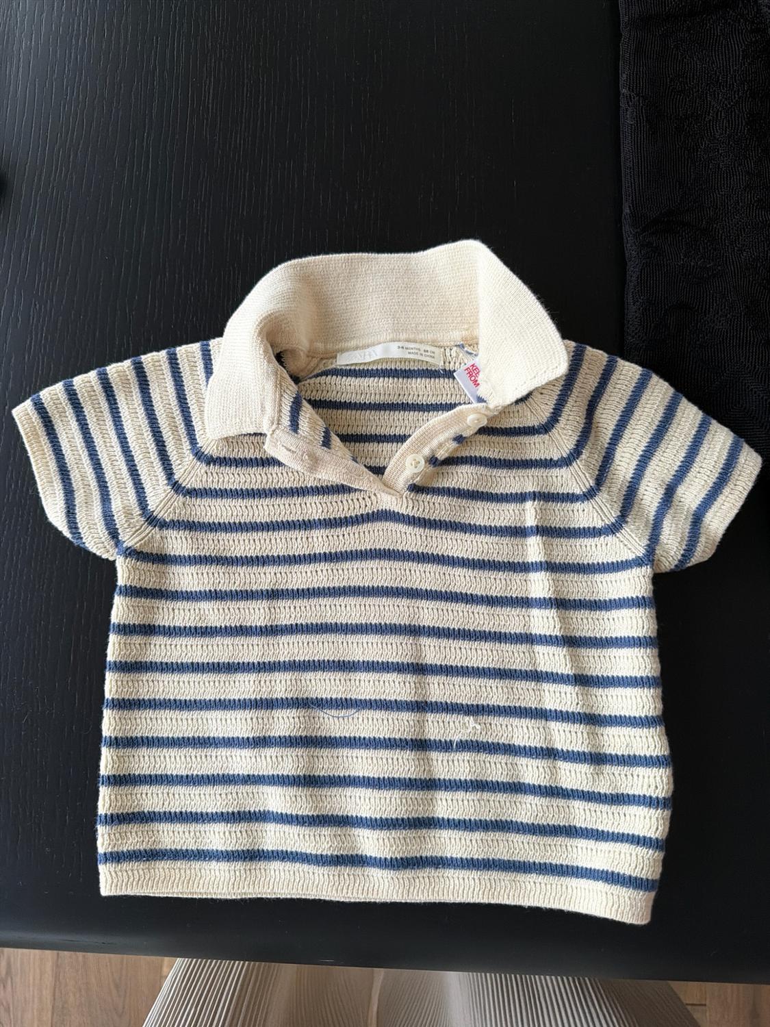 Short-sleeve knit polo with blue and cream stripes over a dark surface. Text: ZARA 3-6 MONTHS 68 CM MADE IN CHINA.