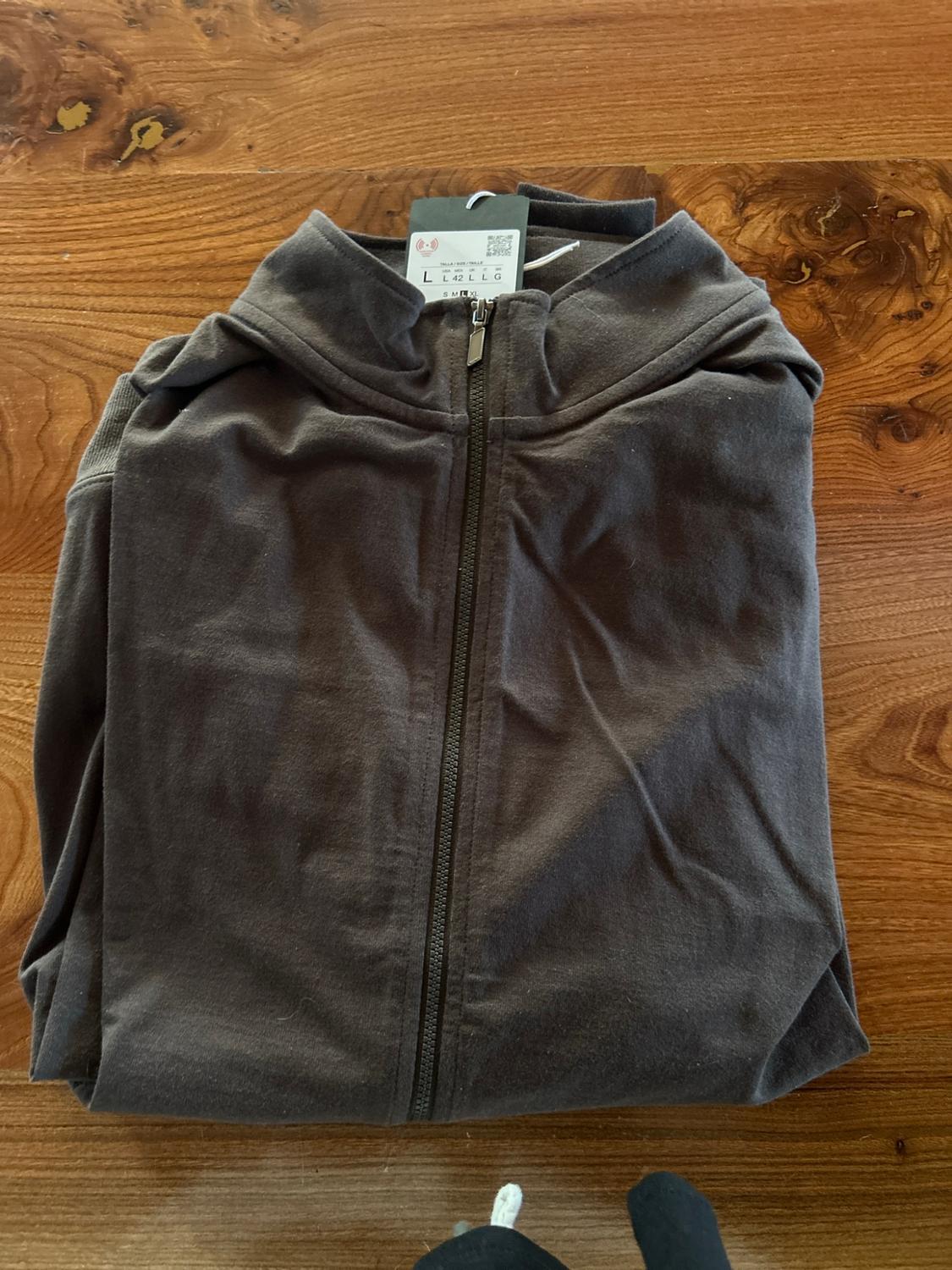 Dark zip-up sweatshirt folded on a wooden table. Visible label with the text L L 42 L L G S M L XL.