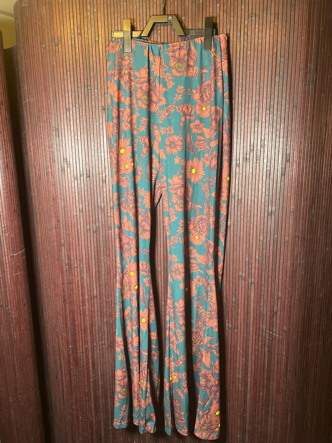 Pants hanging with a floral print in orange and yellow tones on a green background, on a brown wooden panel.