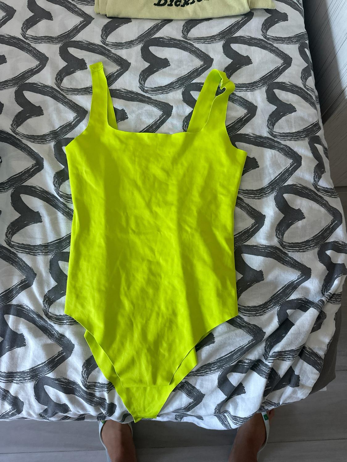 Neon yellow bodysuit on sheets with grey hearts. Peeking out at the top is an item of clothing with the text Dickies and at the bottom are some feet in sandals.