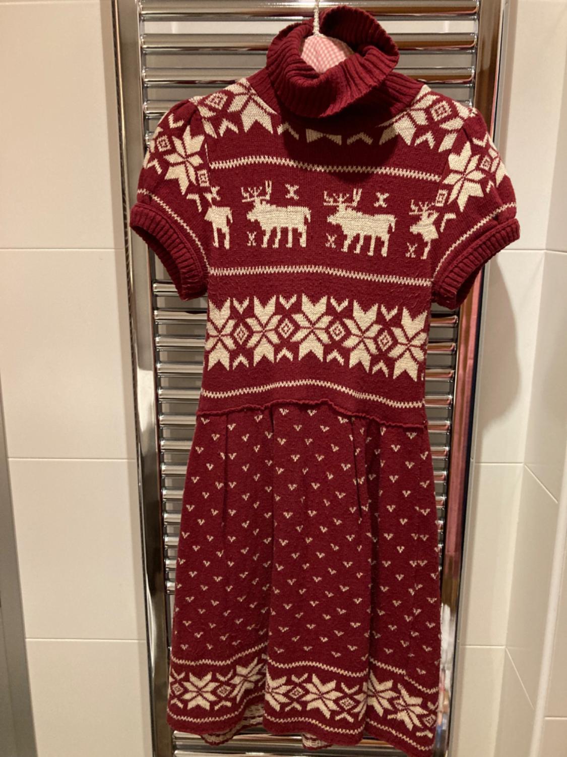 Front view of a red dress with a high neck and a white reindeer and snowflake print.