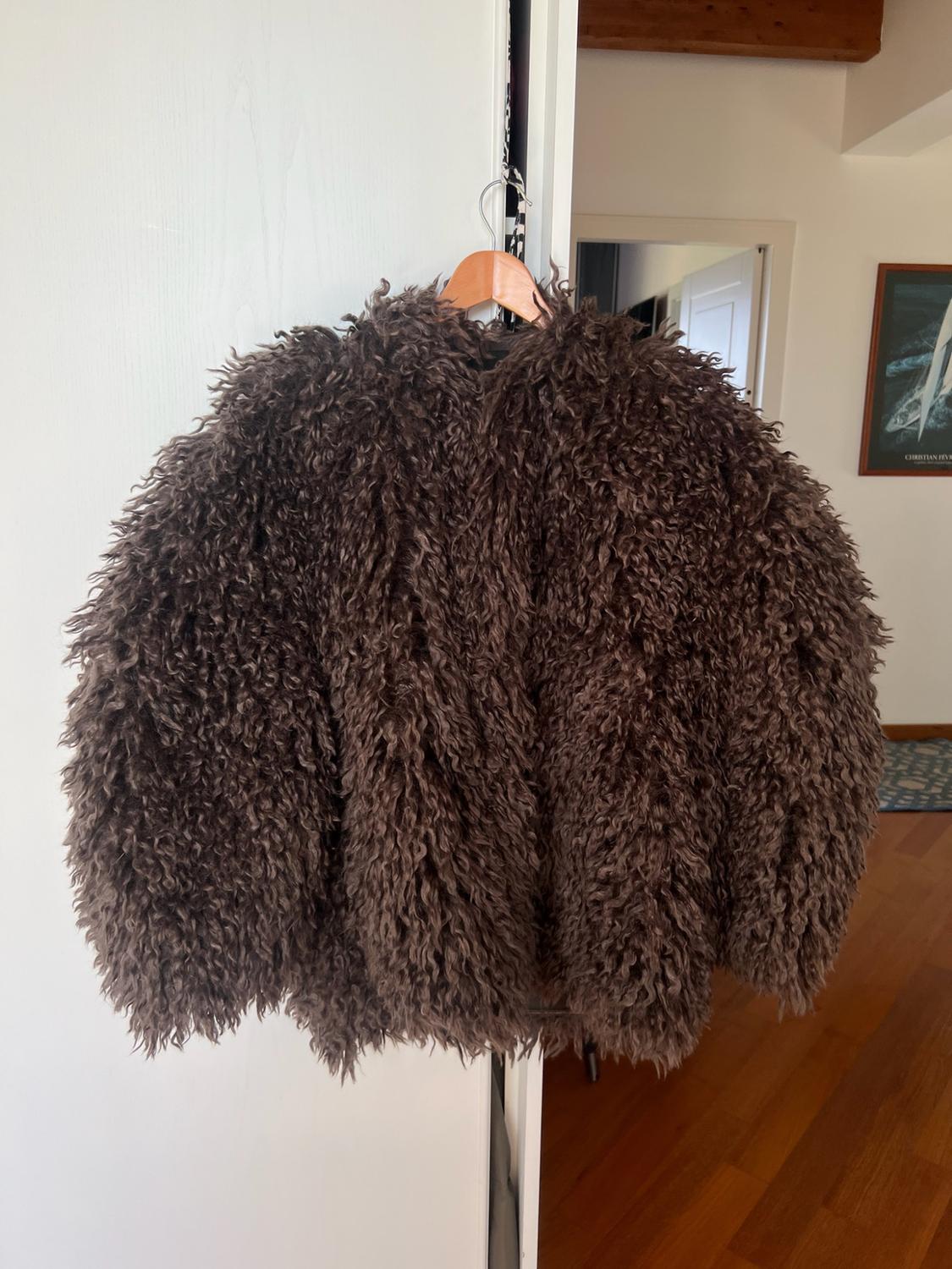 Brown long-hair jacket hanging on a wooden hanger on a white door. In the background, a room with a wooden floor and a painting.