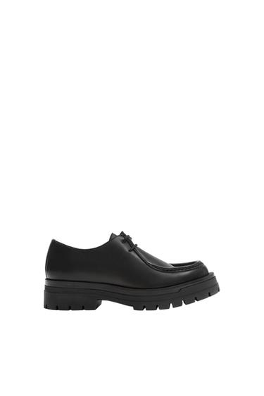 Black lace-up shoe with raised stitching and a chunky lug sole, photographed in profile against a white background.