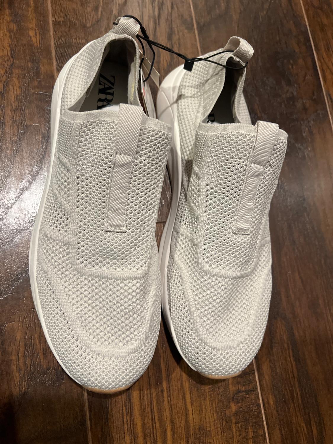 White trainers made of breathable fabric on a wooden floor. Visible label with the text "ZARA" inside.