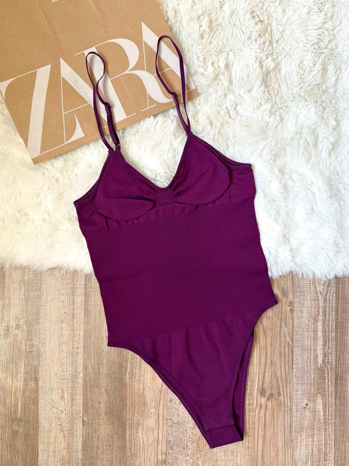 Purple strappy bodysuit on a white rug and wooden floor. A piece of cardboard with the text ZARA can be seen.