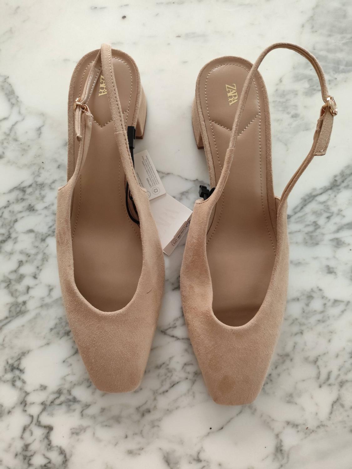 Slingback παπούτσια από μπεζ σουέντ με χαμηλό τακούνι πάνω σε λευκό μάρμαρο. Ορατά κείμενα: ZARA και LEATHER.