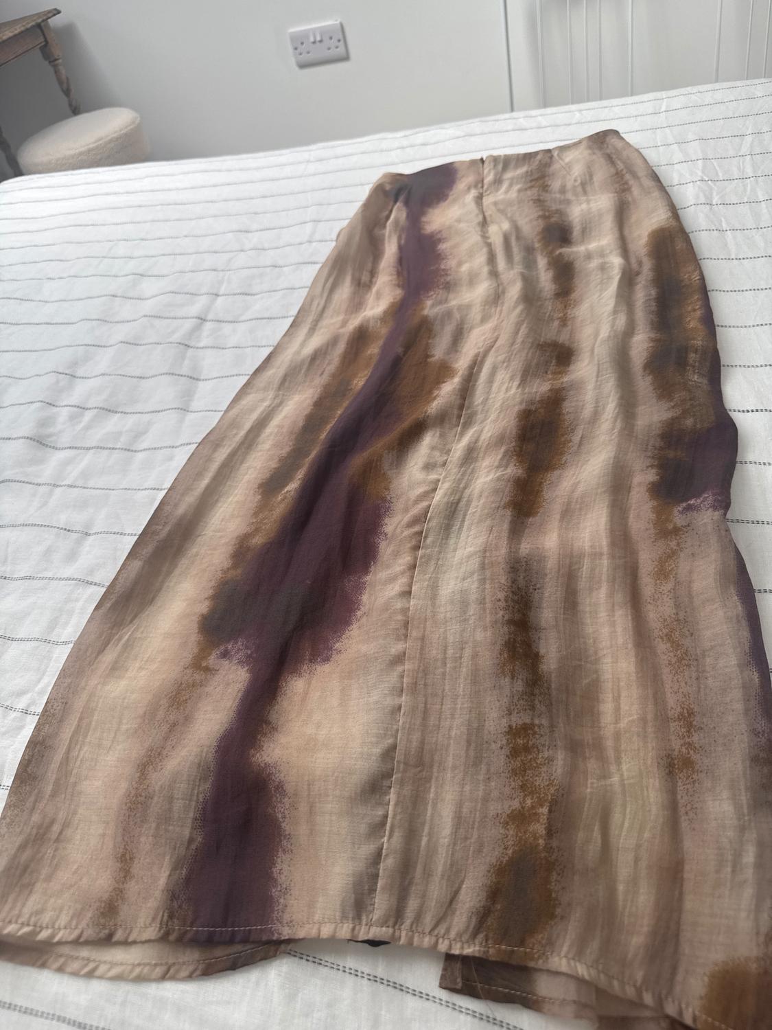 Long skirt with an abstract print in brown and purple tones, on a bed with a white striped bedspread.