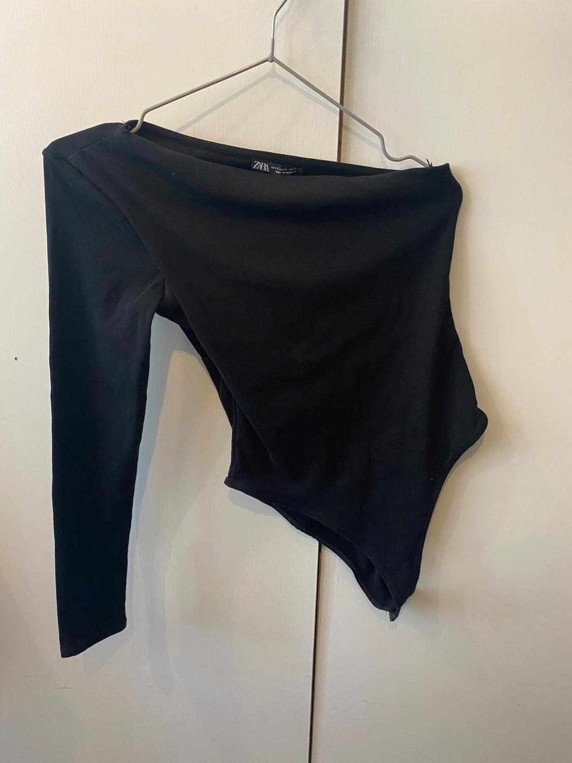 Black long-sleeved bodysuit on a metal hanger against a white background. Visible label with text "Zara".
