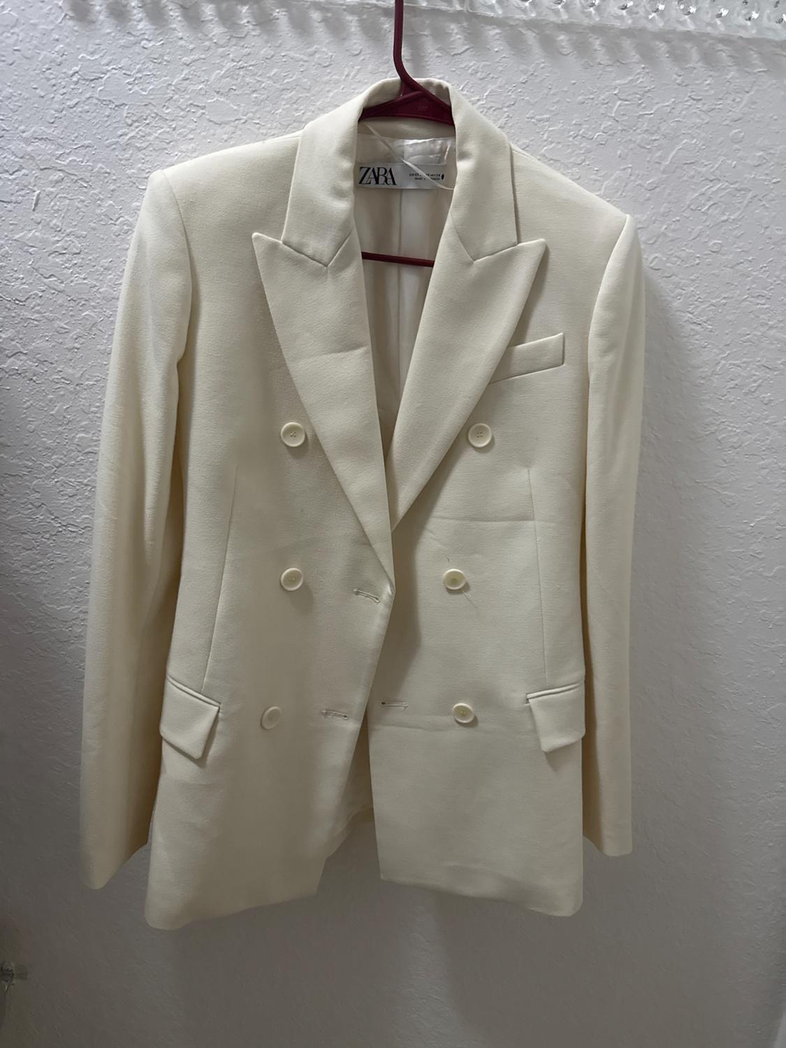 Front view of a white jacket with peak lapels and double-breasted fastening, with flap pockets.