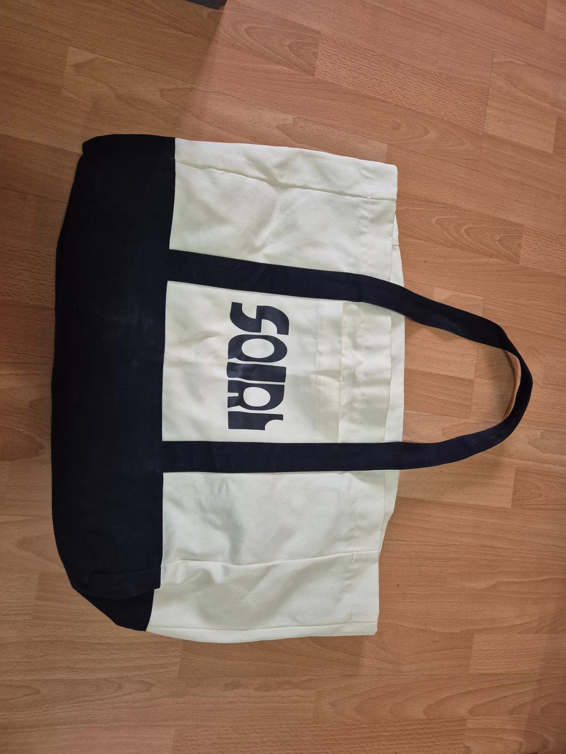 Large white fabric bag with black handles and details, on a wooden floor. Visible text: "SORL".