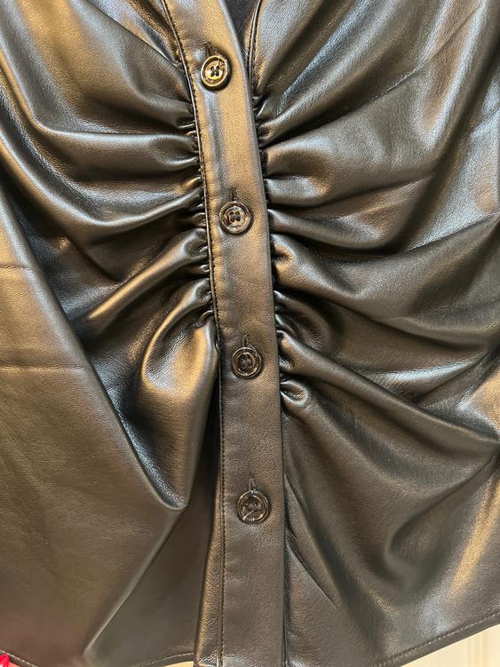 Shiny black fabric with ruffles and buttons in the center. The texture reflects light, creating an elegant and modern effect.
