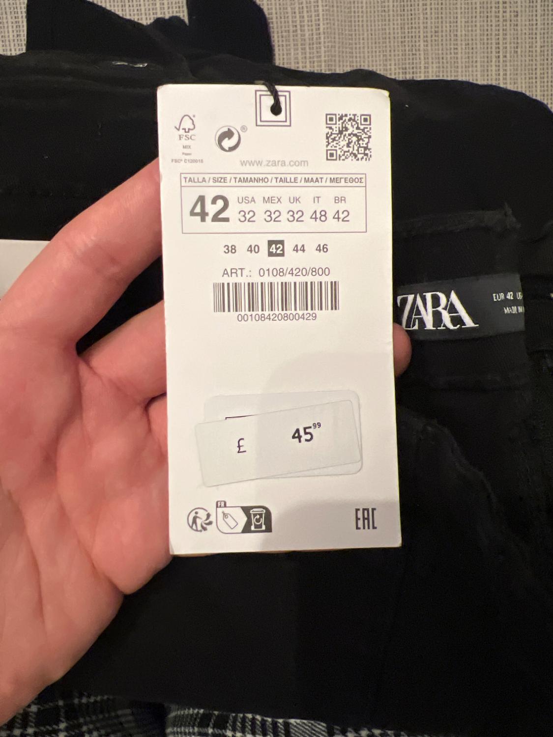 With the Zara label in hand, a size 42 and a price of £45.99 are visible. The barcode and sizing details for different regions are visible.