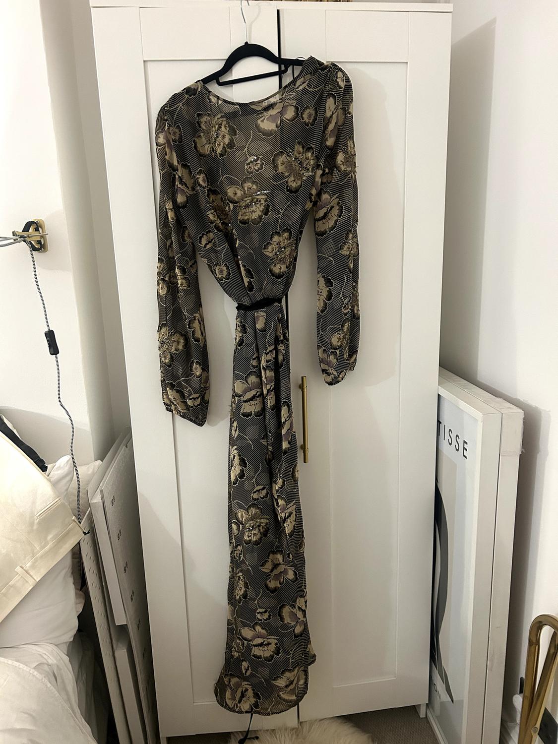 Long dress with a dark-toned floral print, hanging on a black hanger in front of a white wardrobe.