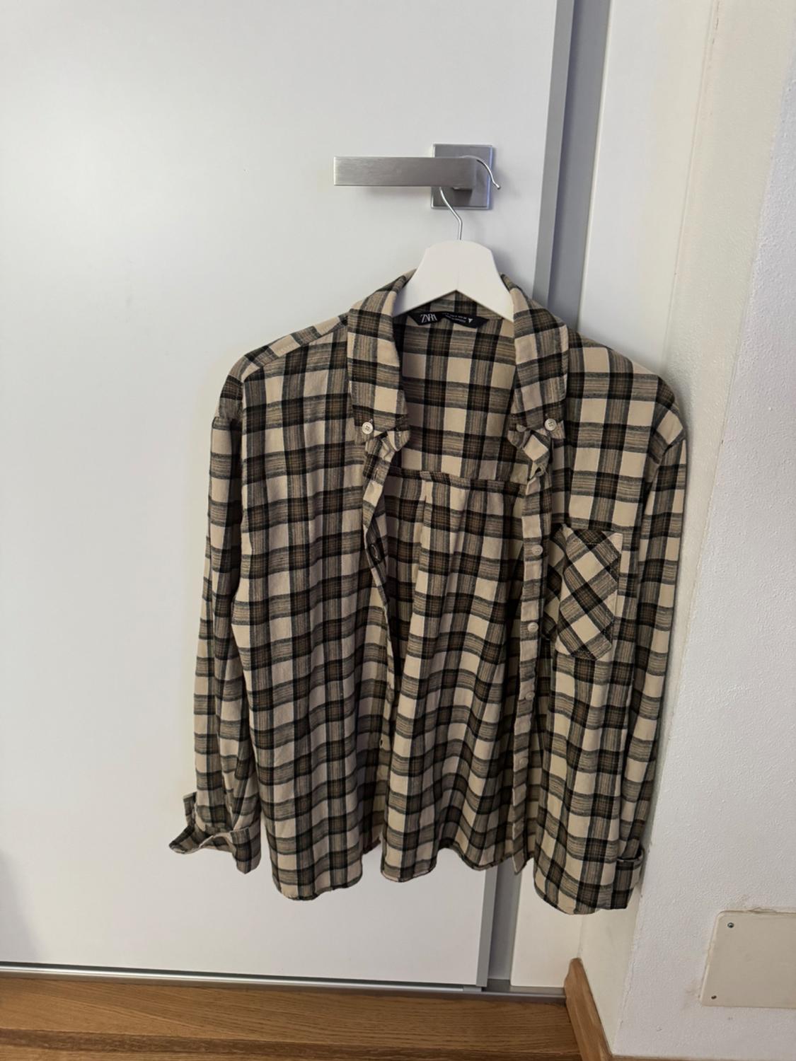 Beige and black checked shirt hanging on a white hanger over a white door. Label with brand visible.