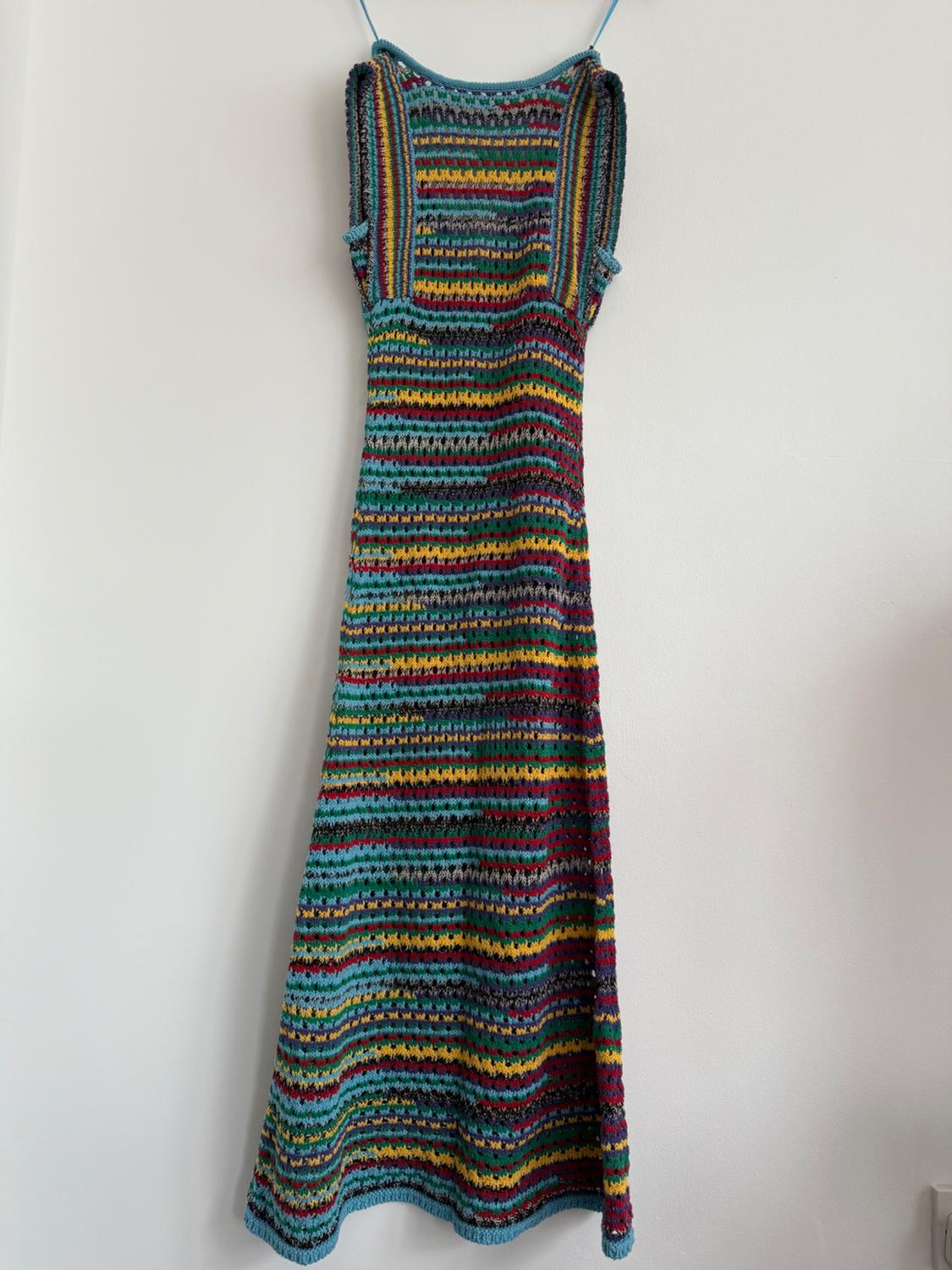 Knitted dress hanging on the wall, with multicoloured stripes in shades of blue, red, yellow and green.