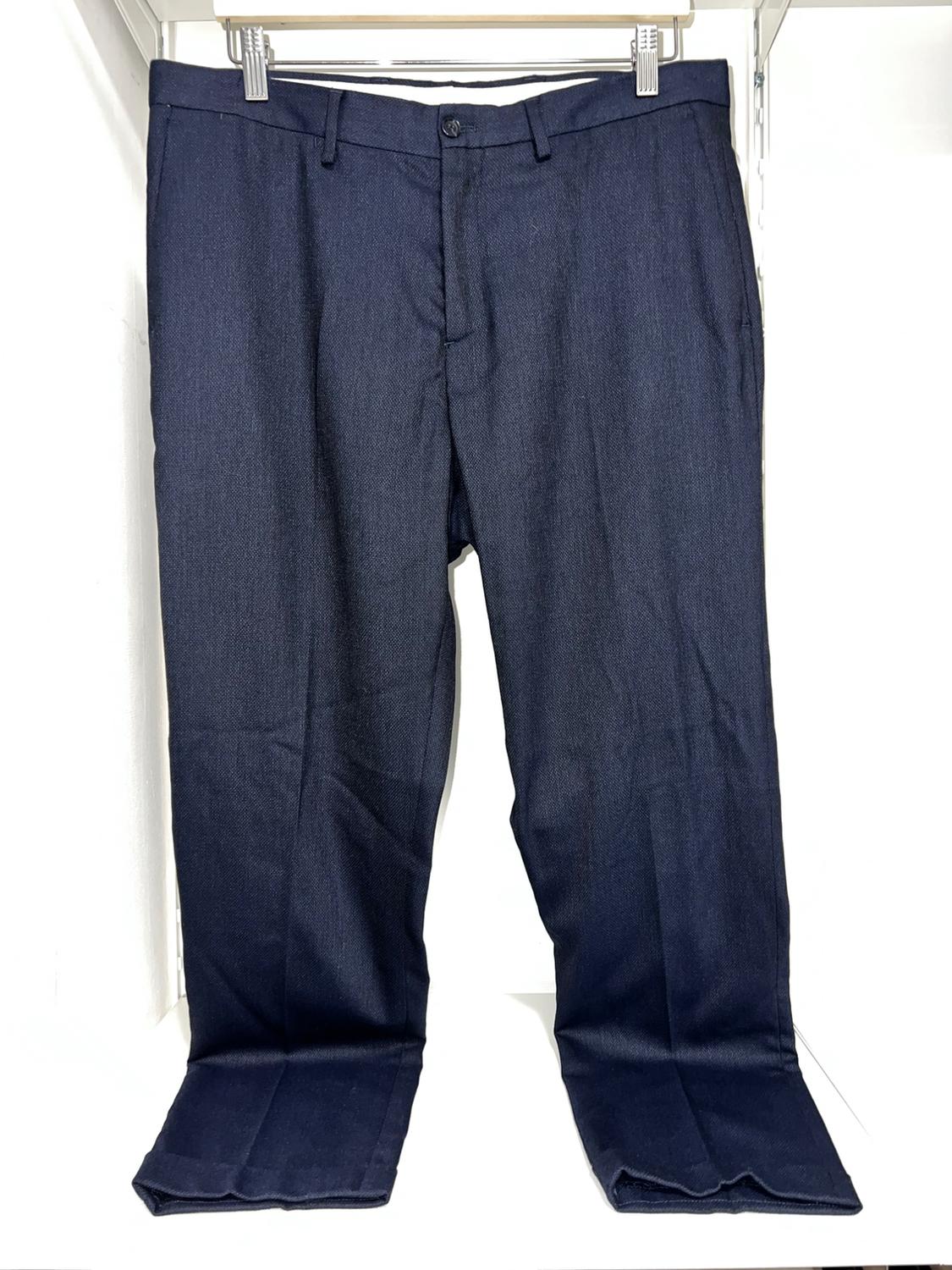 Dark blue trousers hanging on a white hanger, with pleats and a button fastening, against a white background.