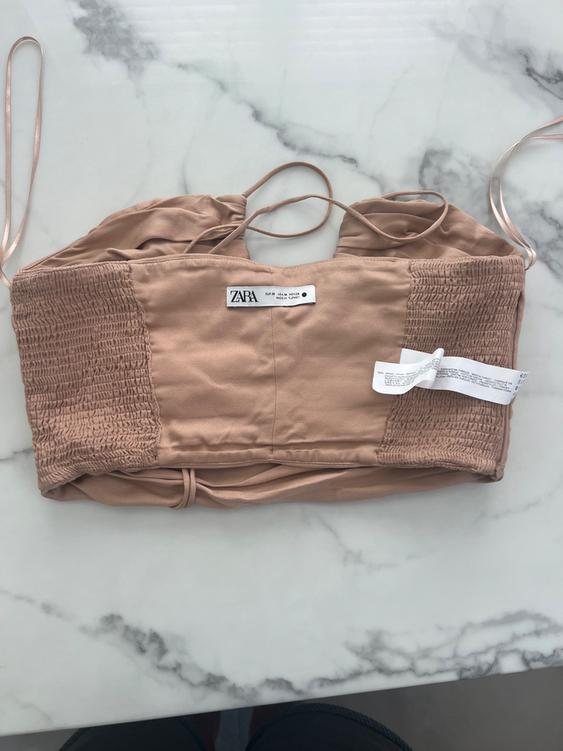 Beige top with thin straps and ruched panels, visible Zara tag, on a white marble background.