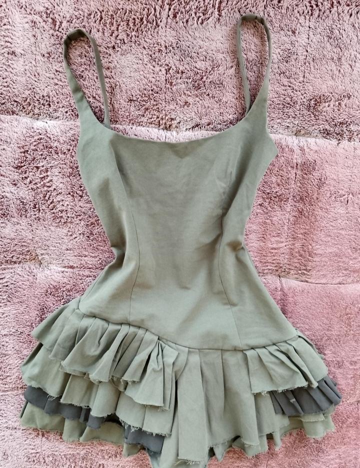 Olive green short strappy dress with a tiered ruffled skirt and a raw hem, on a textured pink blanket.