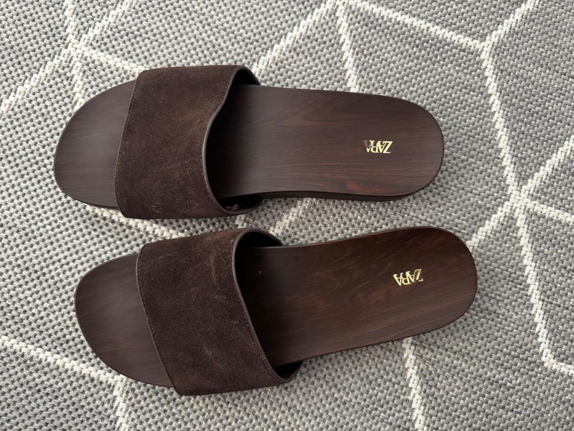 Brown wide-strap sandals with a wood-effect sole on a grey rug with a white geometric pattern. ZARA text on the insole.
