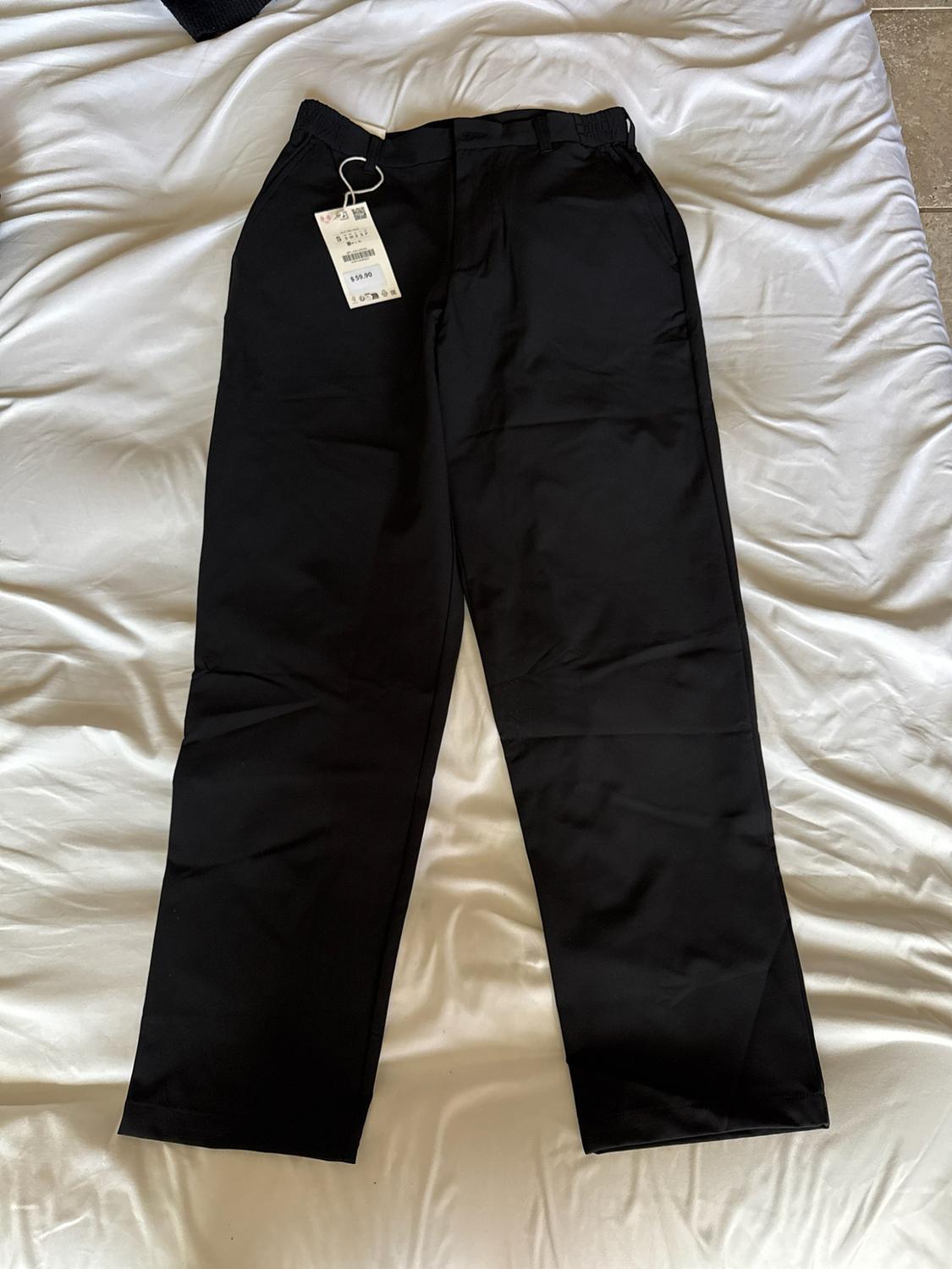 Black trousers with a $59.90 price tag laid out on a crumpled white sheet.