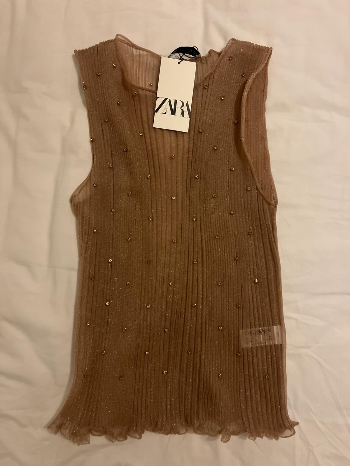 Brown sleeveless top with small sequins, hang tag with text "ZARA", on a white background.