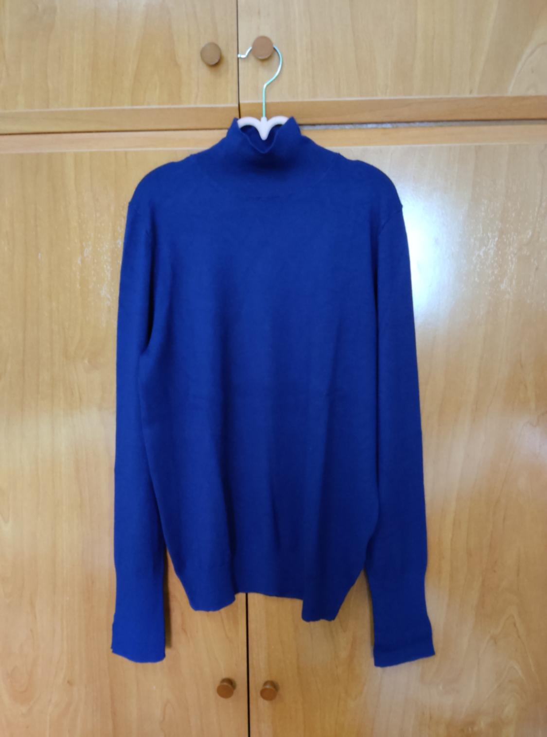 Blue roll-neck jumper hanging on a hanger in front of a light wood wardrobe.