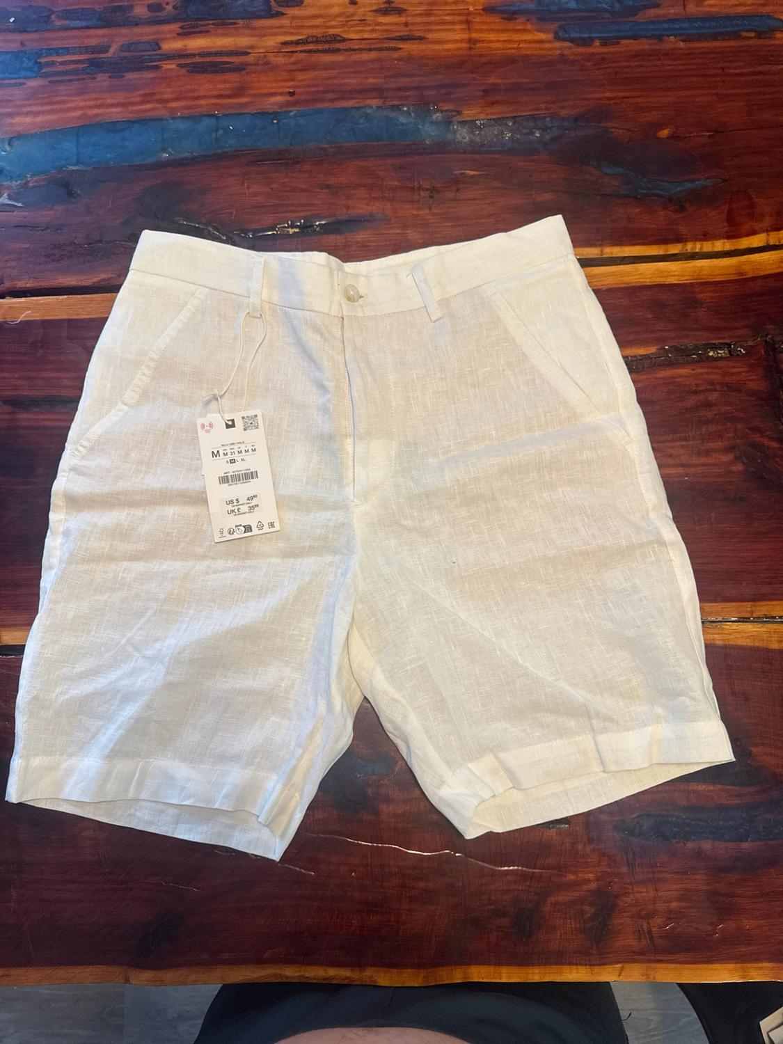 White shorts with pockets and a label, on a rustic wooden table.