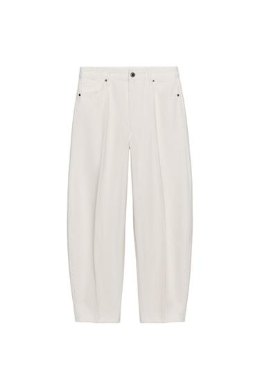 Front view of white baggy trousers with side pockets and front button. Mid-ankle length.