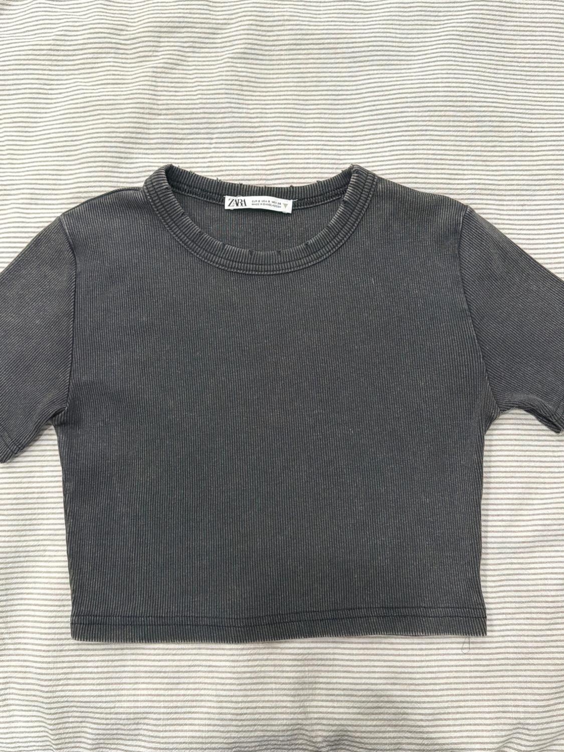 Gray short-sleeved ribbed t-shirt over a striped fabric background. Visible label with text "ZARA".