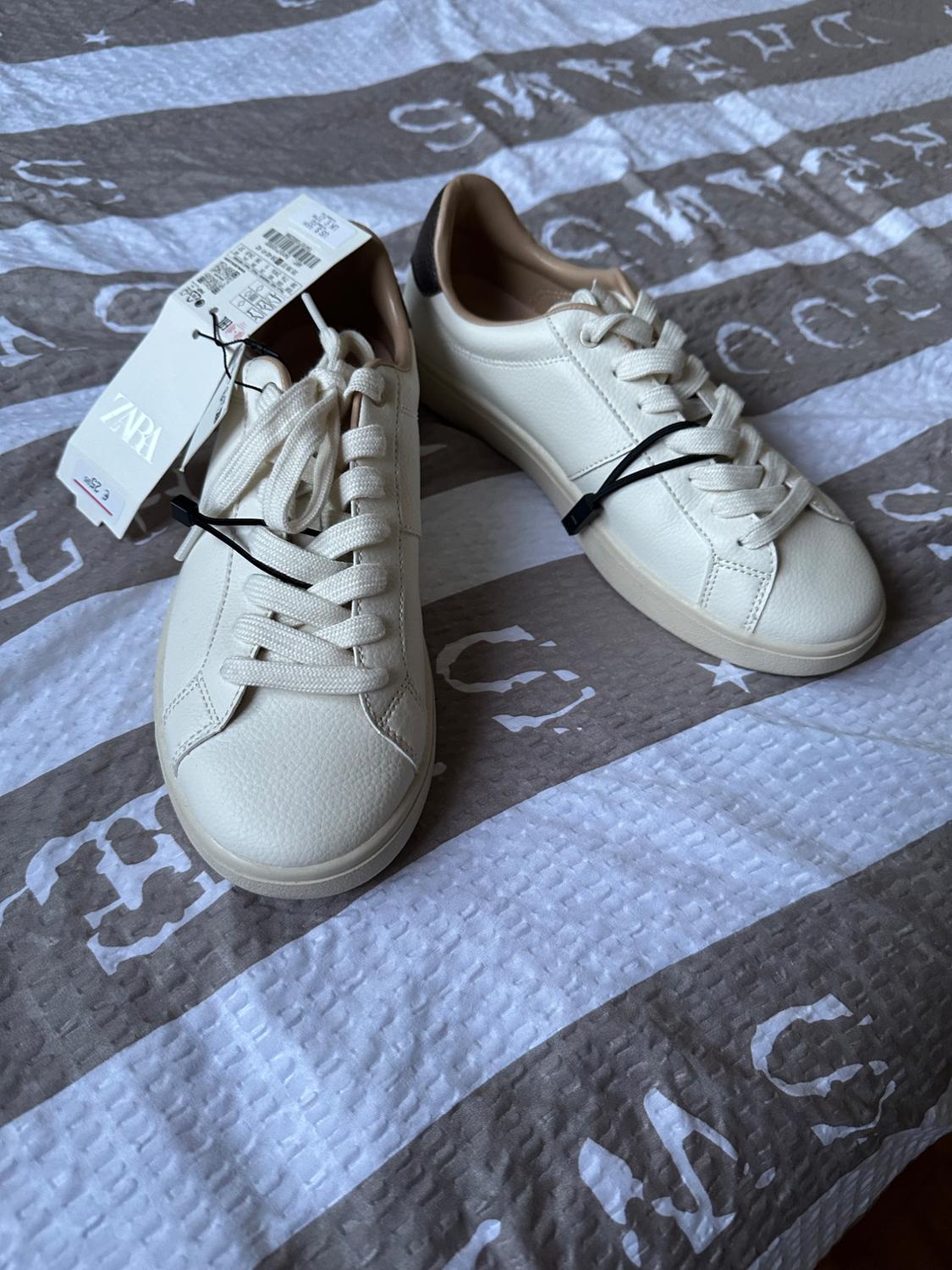 White lace-up trainers with a ZARA label, on a striped fabric with printed lettering. Casual style.