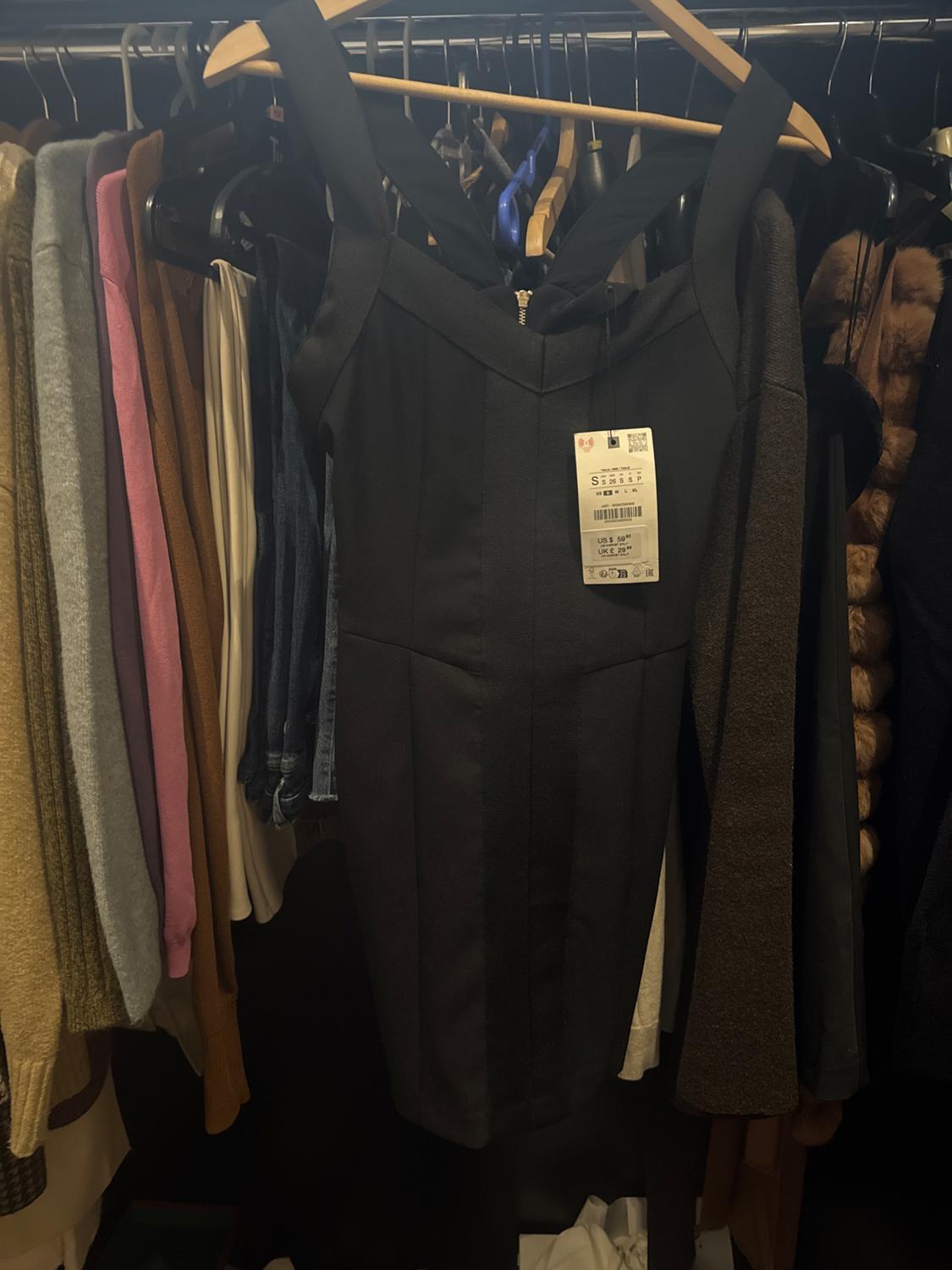 Black strappy dress on a hanger, surrounded by various coloured garments in a wardrobe. Label visible in the centre.