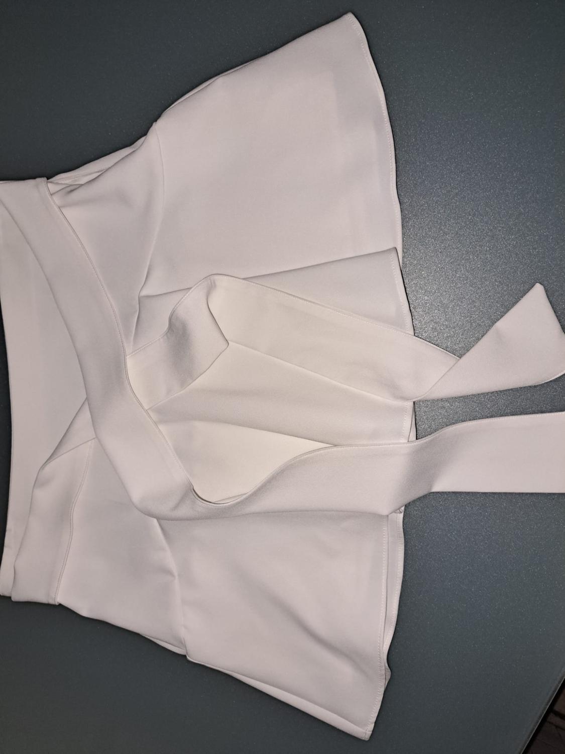 White mini skirt with a bow detail on the waist, laid flat on a smooth dark grey surface.