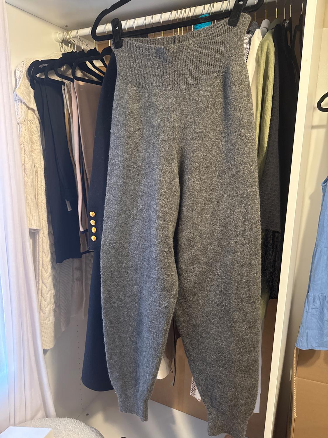 Grey knitted trousers hanging in a wardrobe, surrounded by other garments on hangers. Relaxed and homely atmosphere.