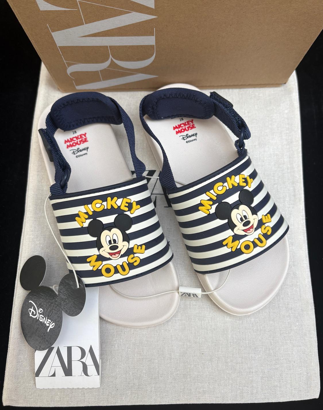 Kids' sandals with a Mickey Mouse design in white and black stripes. Disney and Zara label visible. Box in the background.