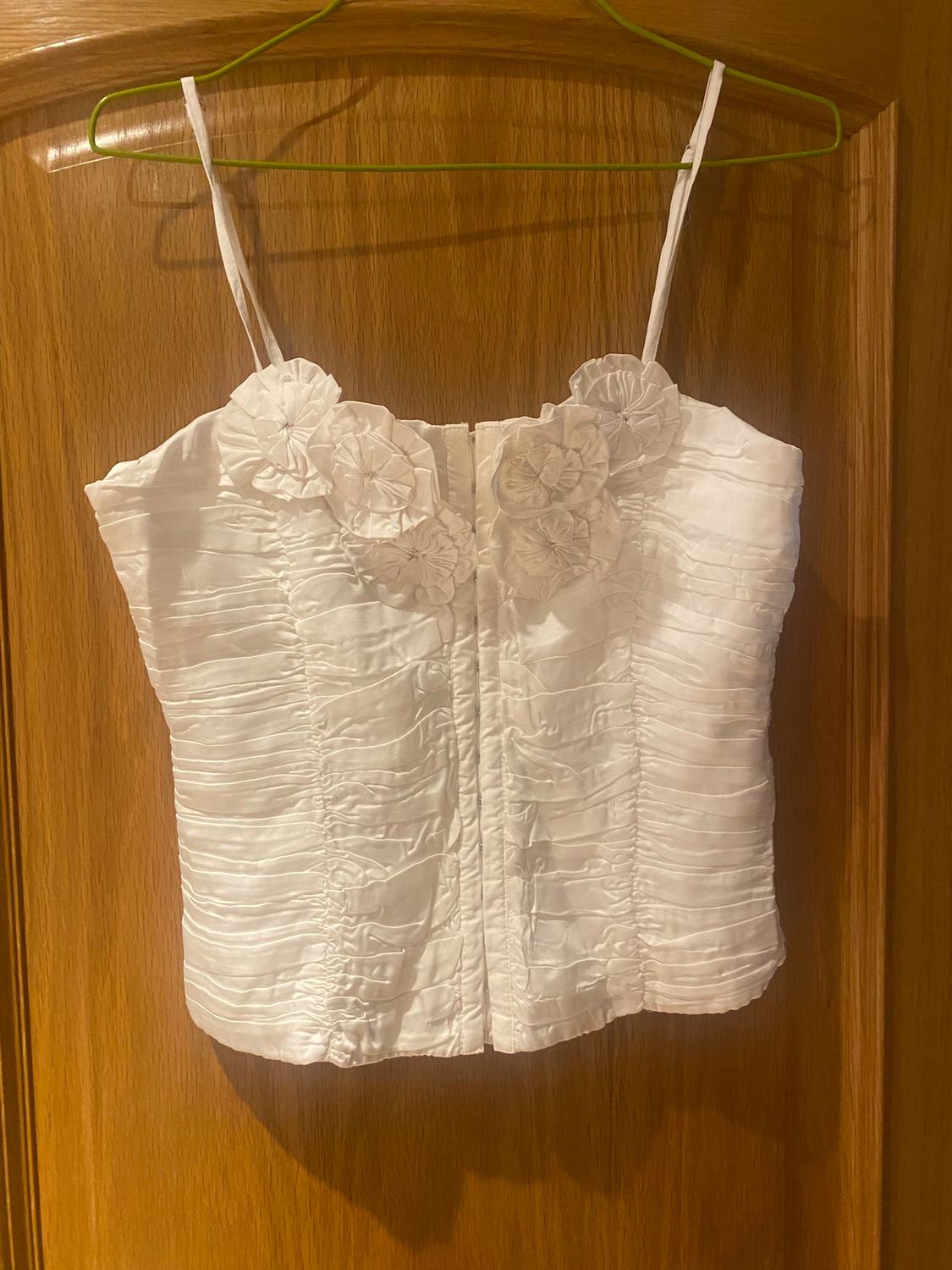 White camisole with thin straps and floral details on the neckline, hanging on a green hanger over a wooden door.