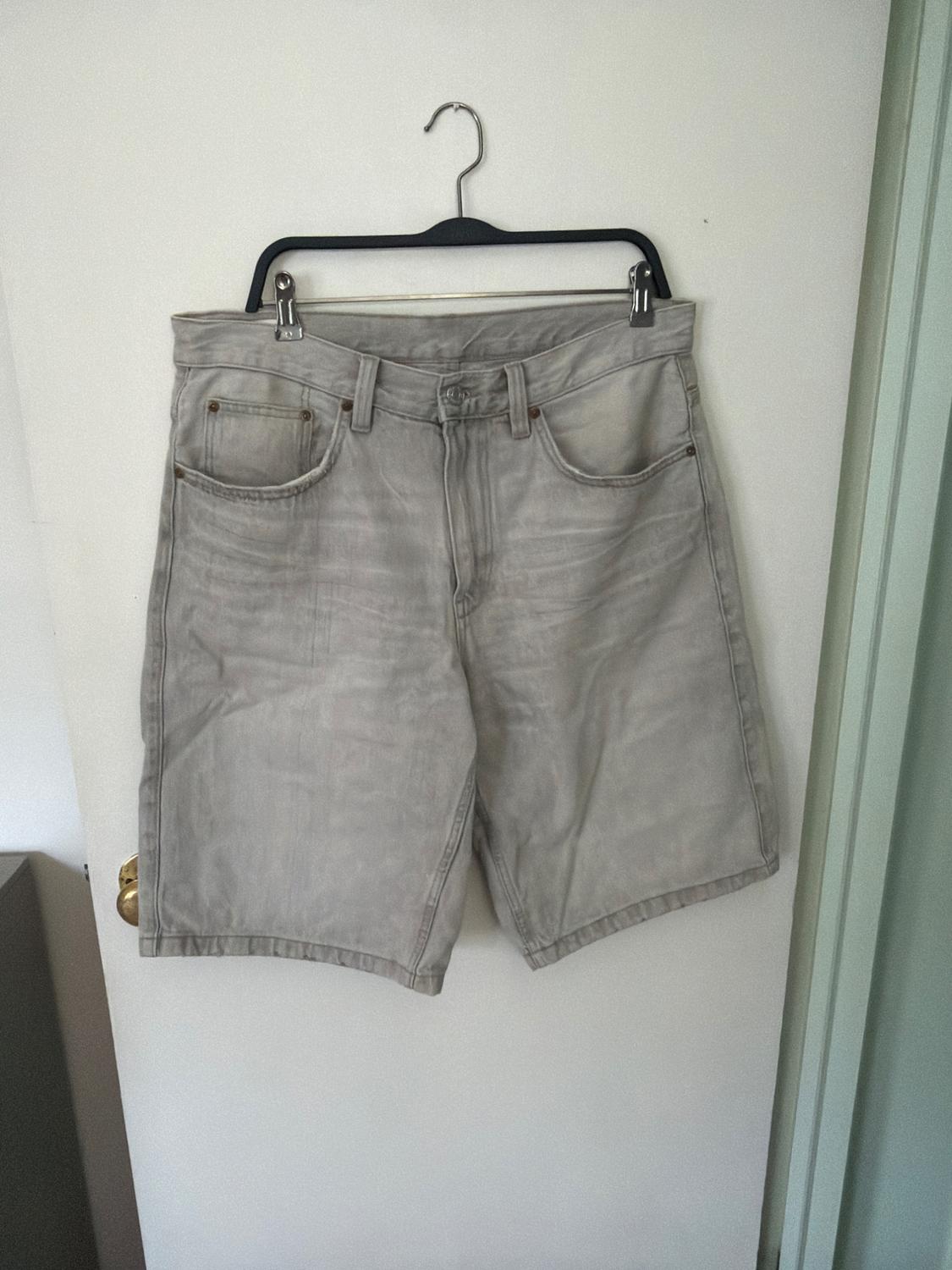 Light gray denim shorts hanging on a black hanger over a white door with a gold doornob.